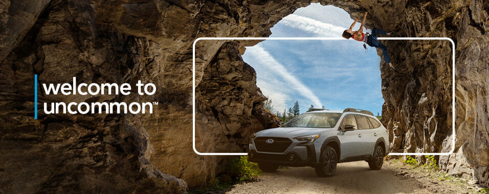 A 2023 Subaru Outback sits underneath as rock climber carefully climbs a cave.